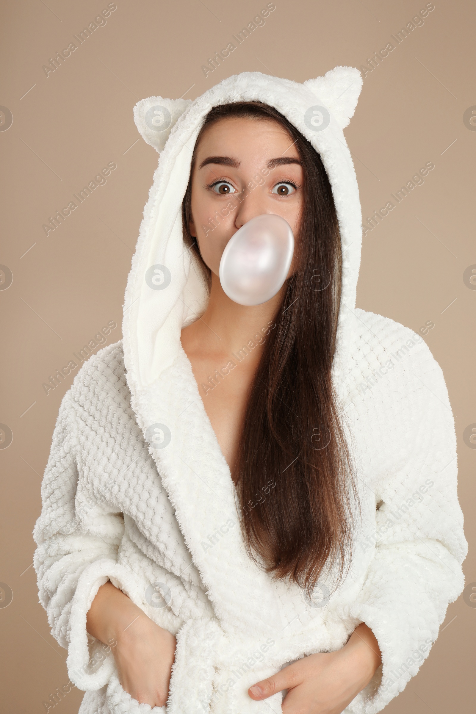 Photo of Young woman in bathrobe blowing chewing gum on brown background