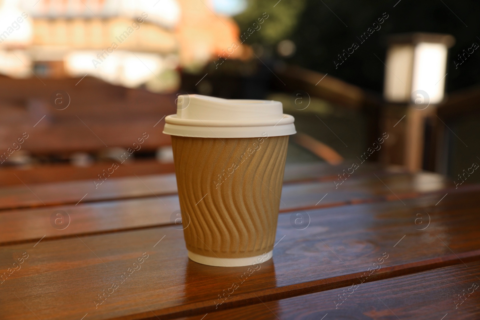 Photo of Takeaway paper cup with coffee on wooden table outdoors