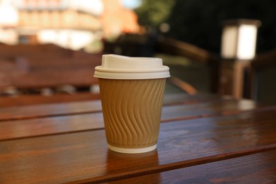 Photo of Takeaway paper cup with coffee on wooden table outdoors