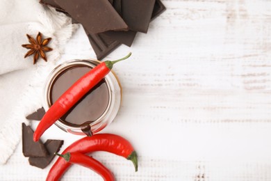 Glass of hot chocolate with chili pepper on white wooden table, flat lay. Space for text