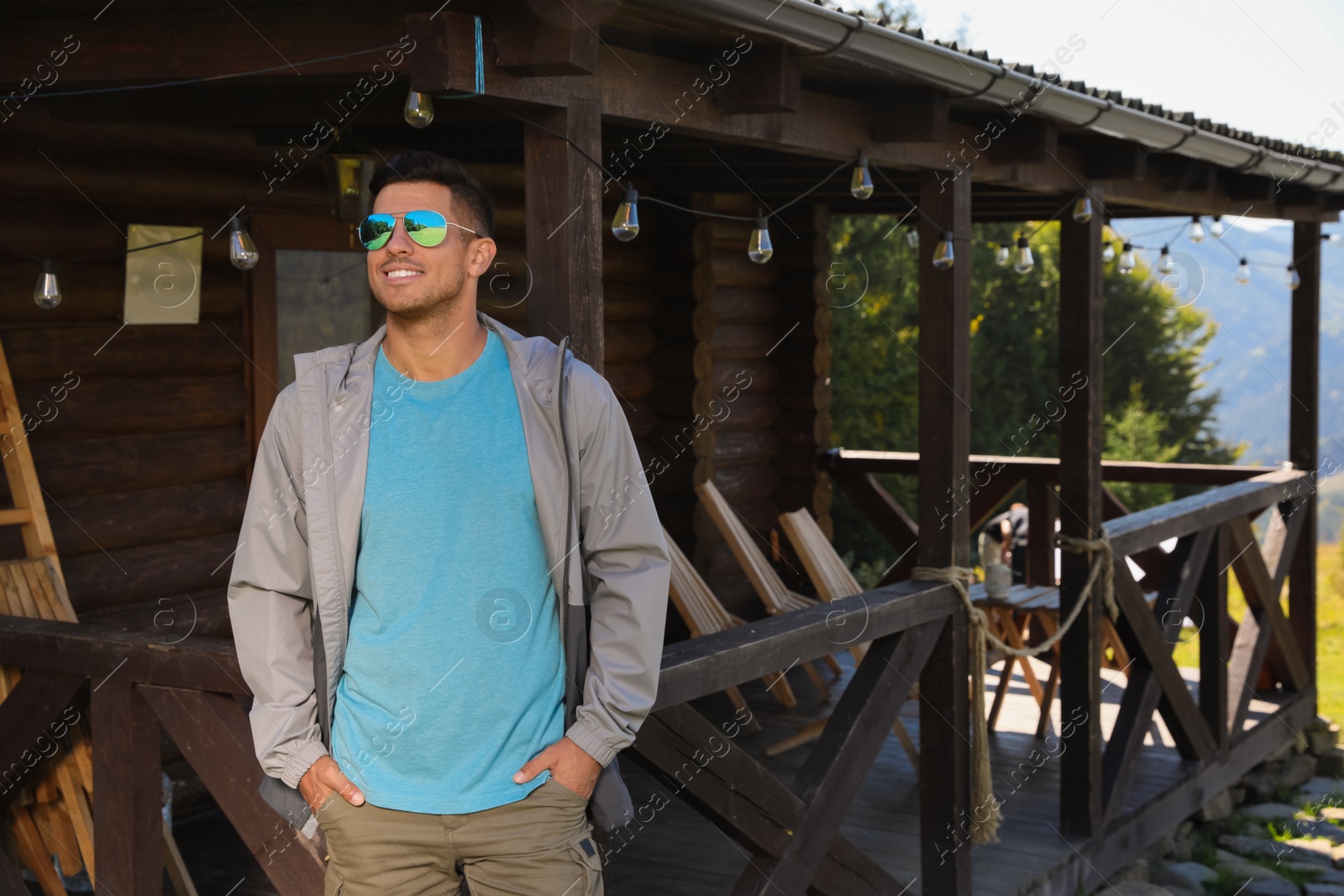 Photo of Handsome man enjoying beautiful nature near house with wooden terrace