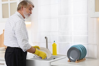 Photo of Senior man in protective gloves washing plate above sink in kitchen, space for text