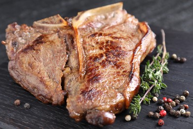 Delicious fried beef meat, thyme and peppercorns on wooden board, closeup