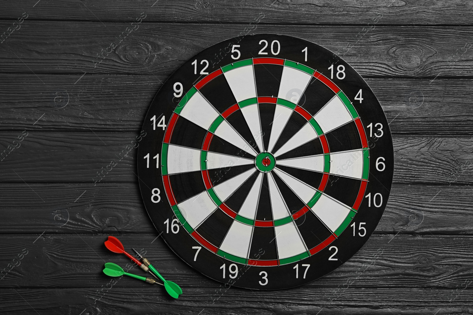 Photo of Dart board with color arrows on black wooden background, top view