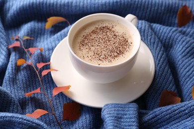 Cup of hot drink and leaves on blue knitted sweater. Cozy autumn atmosphere