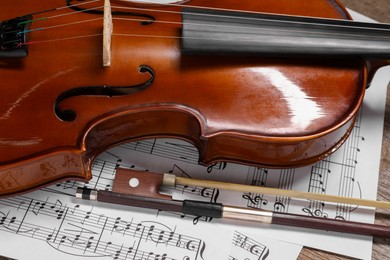 Photo of Violin, bow and music sheets on wooden table, closeup
