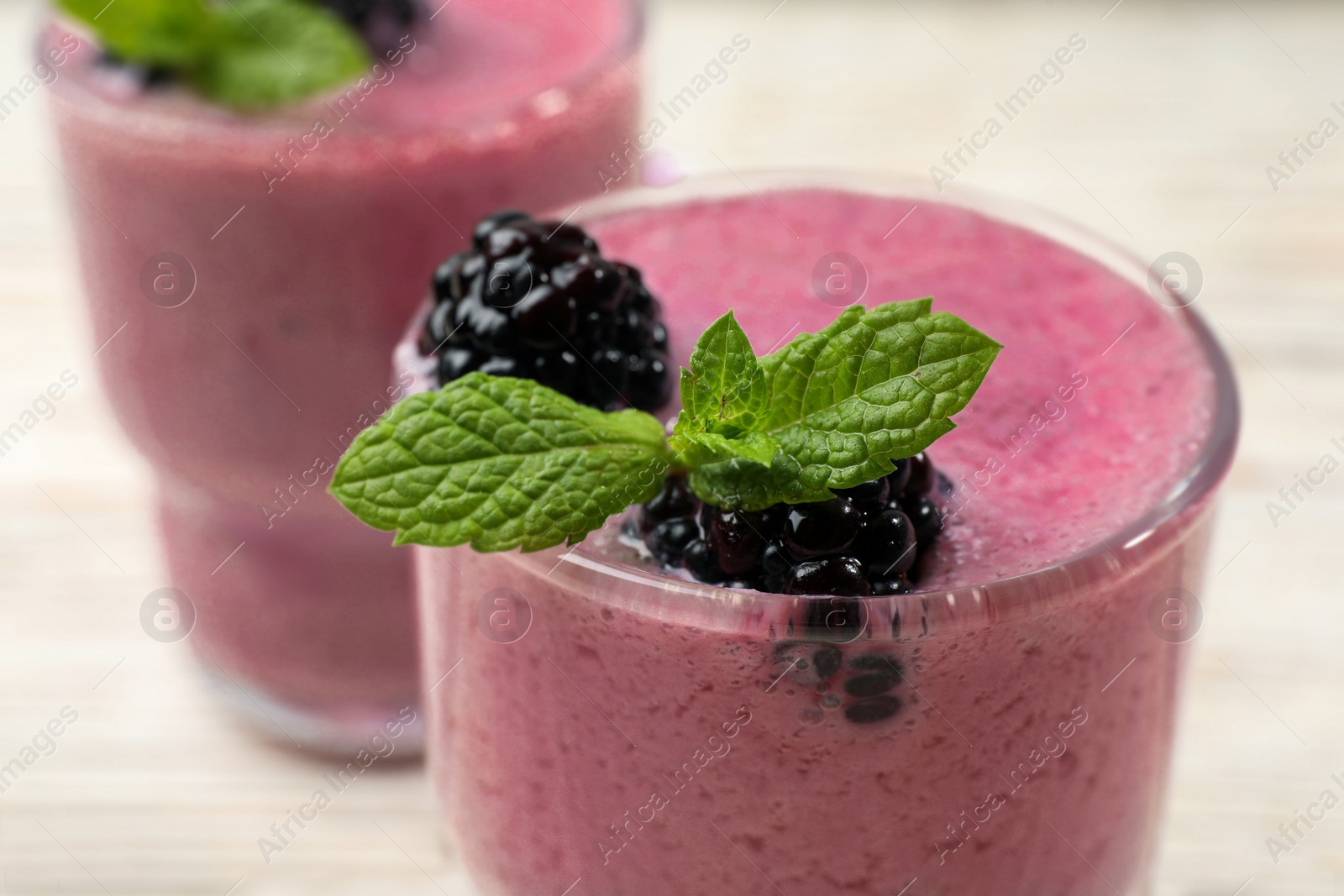 Photo of Glass of blackberry smoothie with mint and berries on light table, closeup