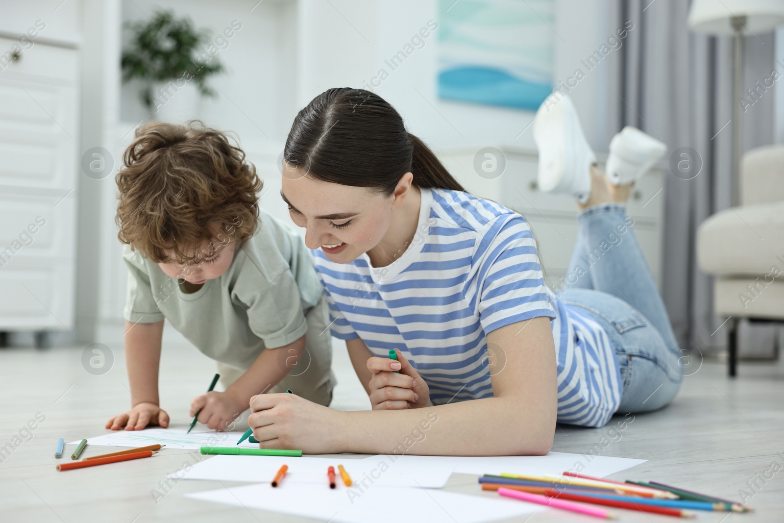 Photo of Mother and her little son drawing with colorful markers on floor at home