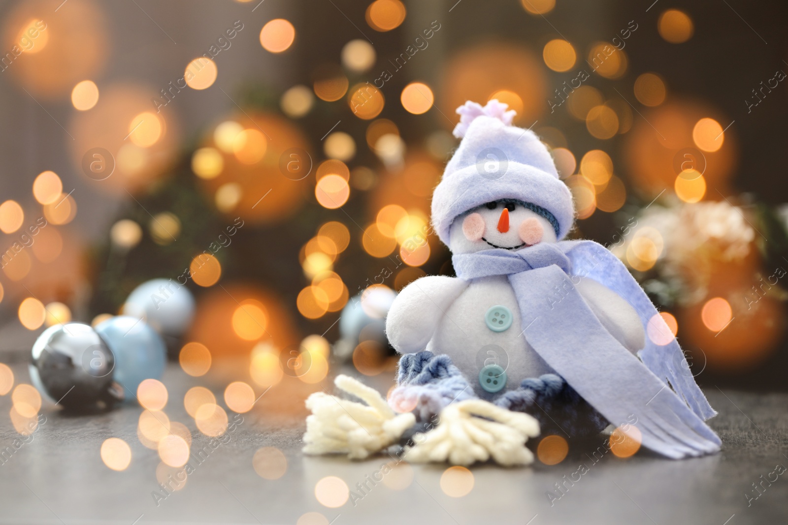 Image of Cute snowman and Christmas balls on table, bokeh effect