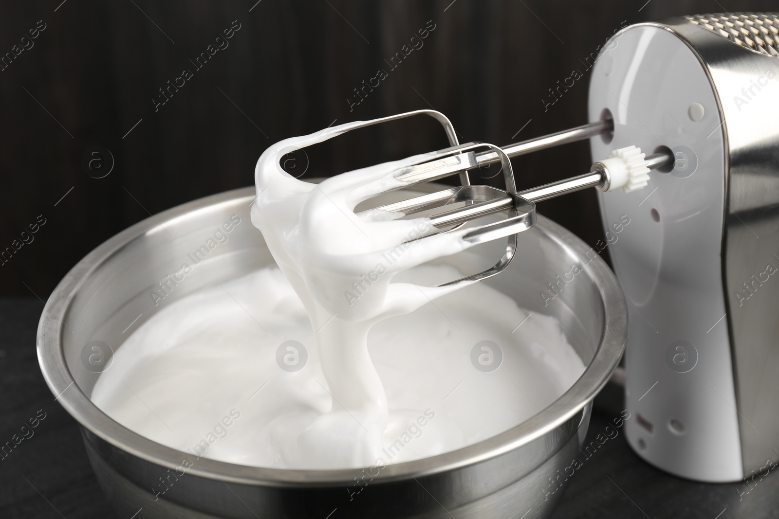 Photo of Bowl with whipped cream and hand mixer on black background, closeup