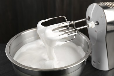 Bowl with whipped cream and hand mixer on black background, closeup