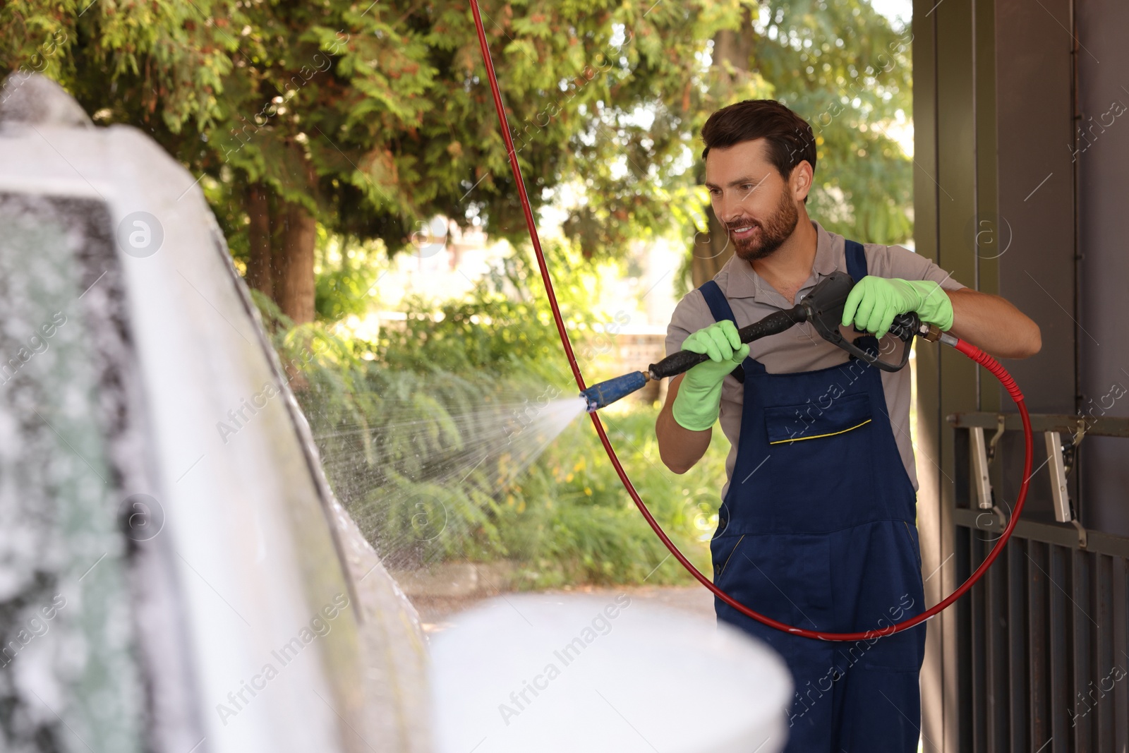 Photo of Worker washing auto with high pressure water jet at outdoor car wash