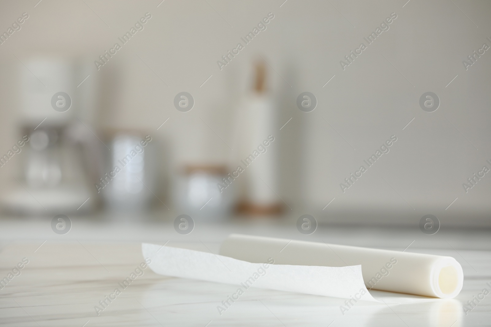 Photo of Roll of baking paper on white marble table against blurred background indoors. Space for text