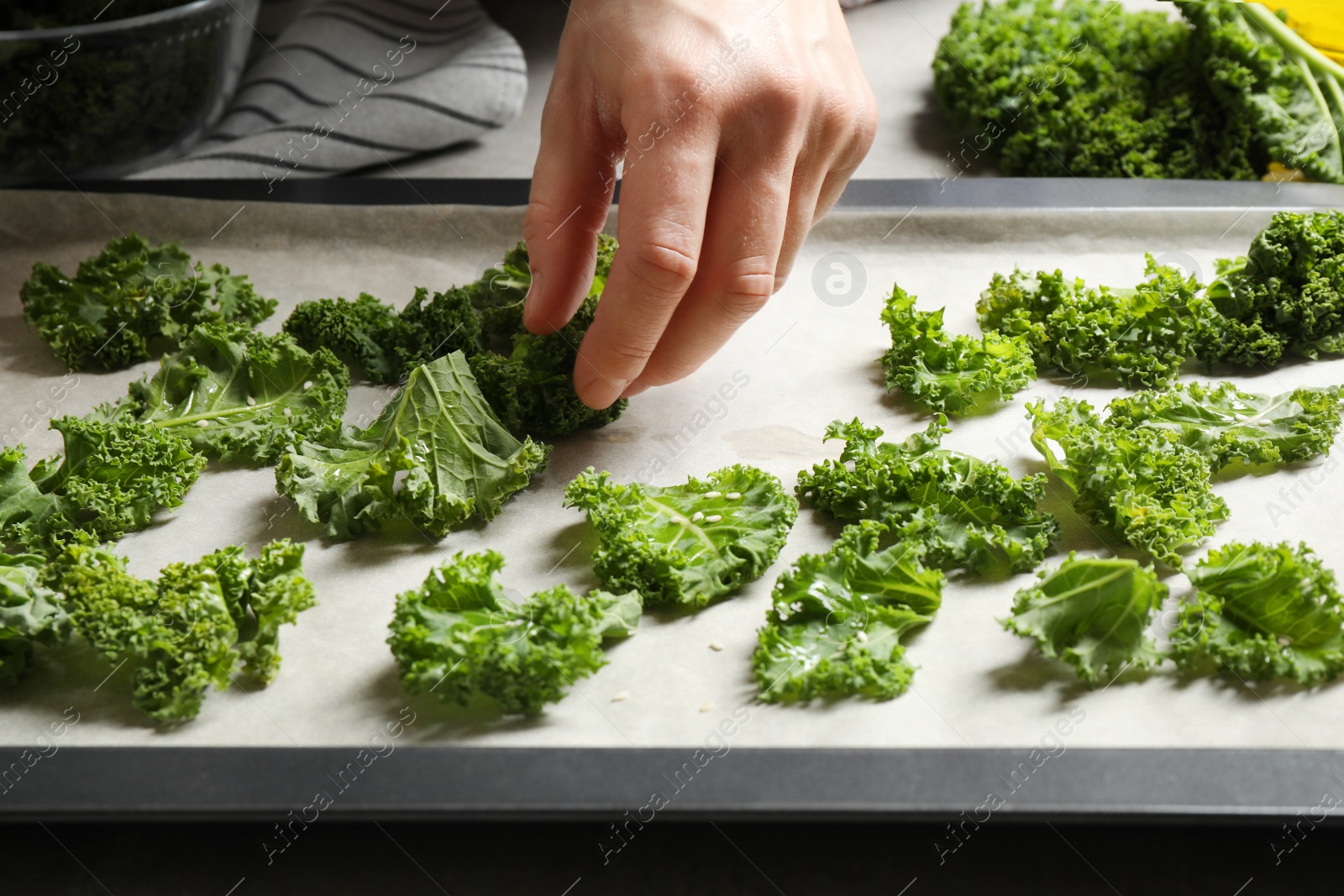 Photo of Woman preparing kale chips at table, closeup