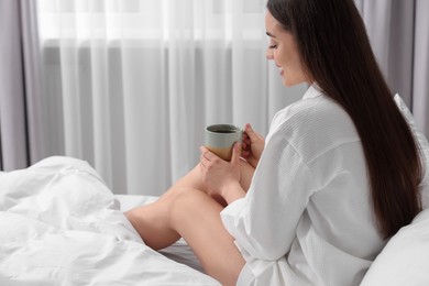 Happy woman with cup of drink on bed at home, space for text. Lazy morning