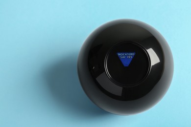 Photo of Magic eight ball with prediction Indications Say Yes on light blue background, top view. Space for text