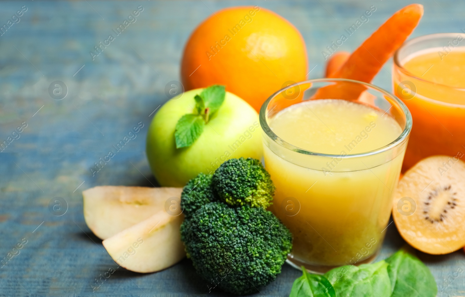 Photo of Glasses of delicious juices and fresh ingredients on blue wooden table, closeup. Space for text