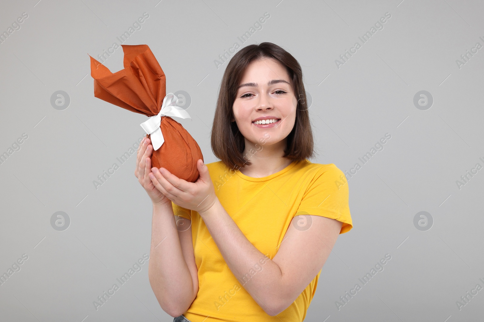 Photo of Easter celebration. Happy woman with wrapped egg on grey background