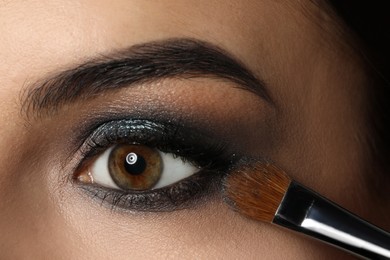 Photo of Applying dark eye shadow with brush onto woman's face, closeup. Beautiful evening makeup