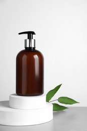 Photo of Bottle of cosmetic product and green leaves on light grey table against white background