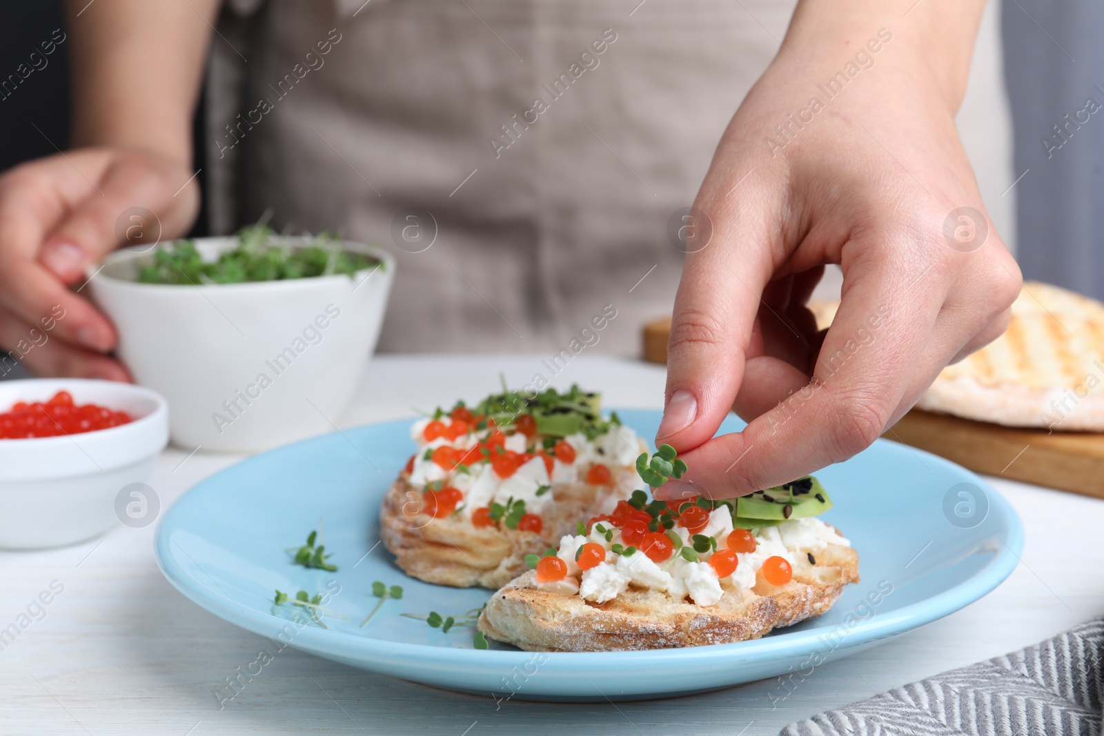 Photo of Woman putting microgreens onto sandwich with caviar at table, closeup