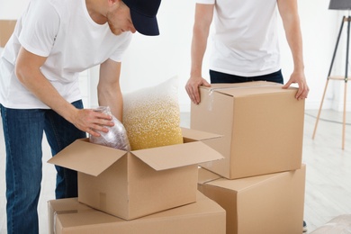 Moving service employees with cardboard boxes and belongings in room, closeup