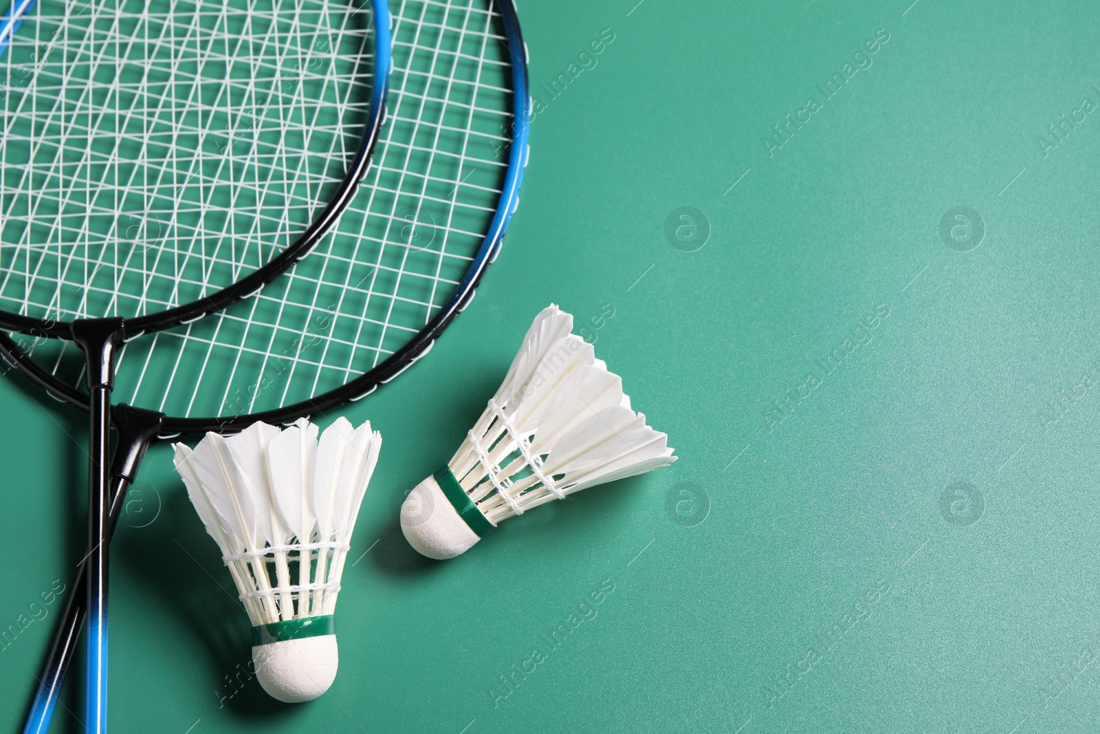Photo of Feather badminton shuttlecocks and rackets on green background, flat lay. Space for text