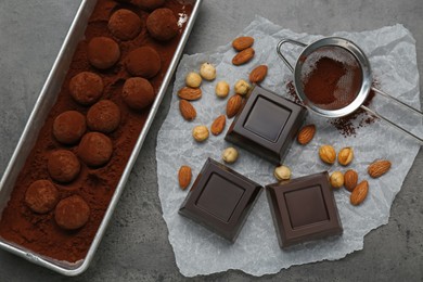 Delicious chocolate candies powdered with cocoa, sieve and ingredients on grey table, flat lay