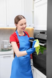 Photo of Woman cleaning electric oven with rag in kitchen