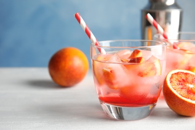 Glass of tropical cocktail with ice cubes on table against color background. Space for text