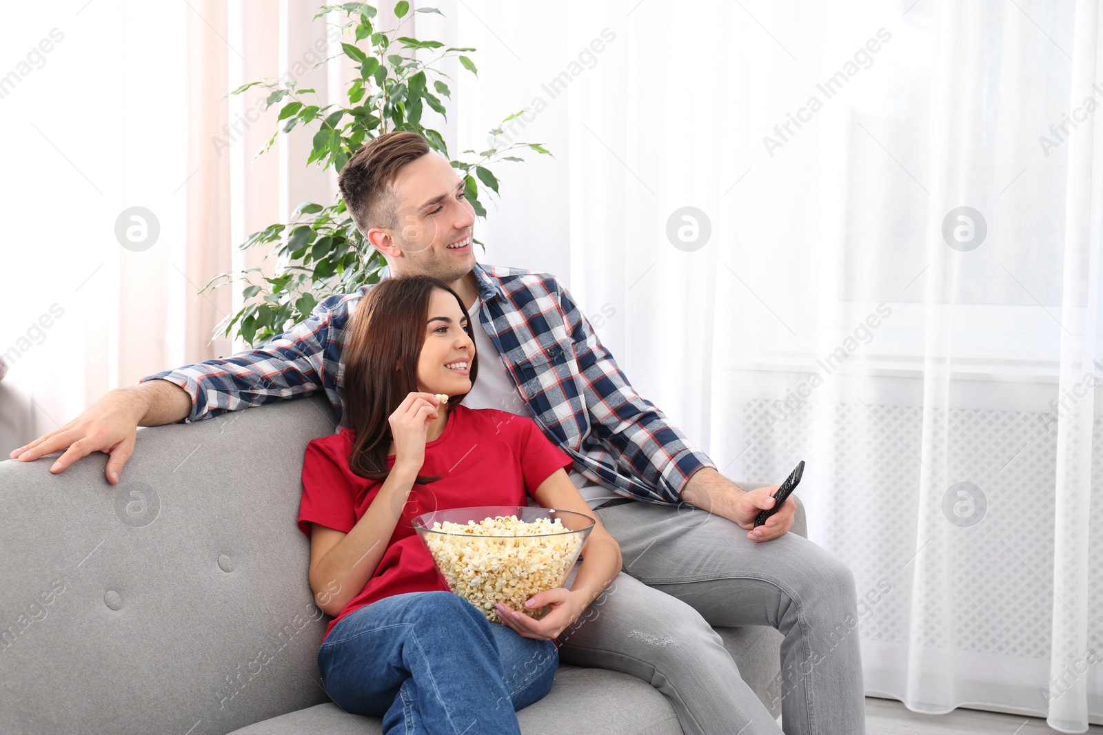 Photo of Happy young couple watching TV on sofa at home