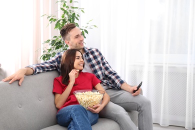 Happy young couple watching TV on sofa at home