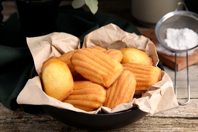 Delicious madeleine cakes in bowl on wooden table