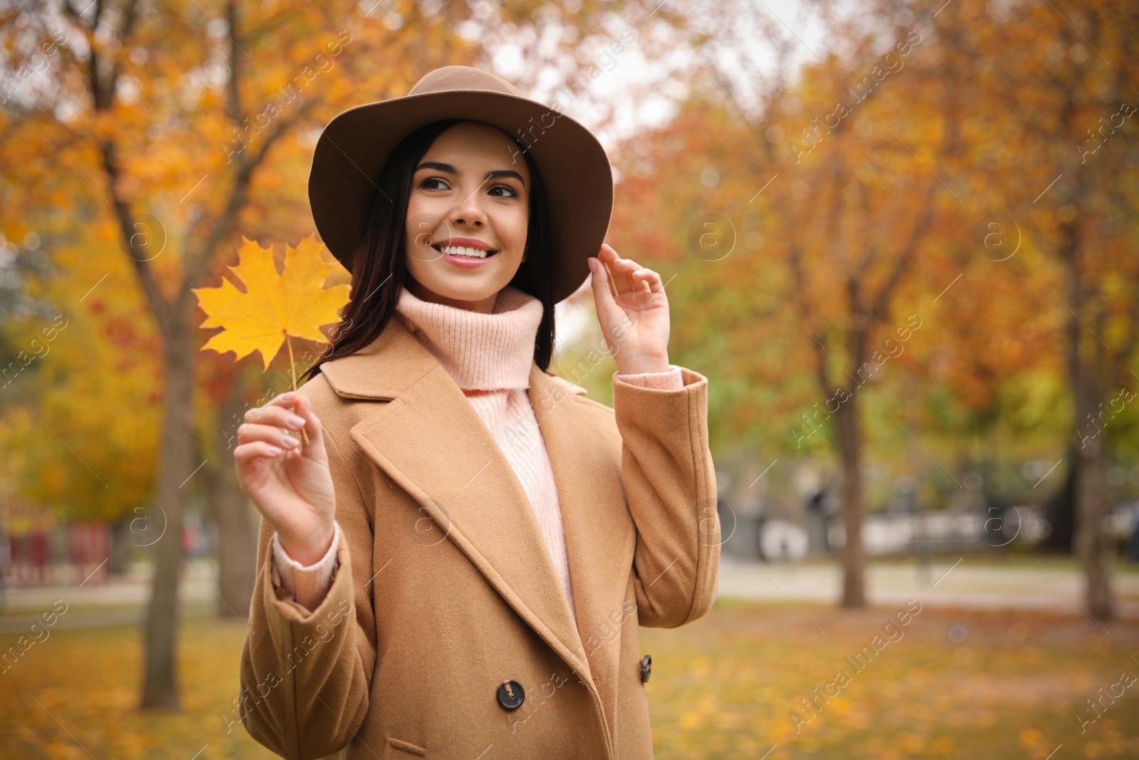 Photo of Young woman in stylish clothes holding yellow leaf outdoors. Autumn look