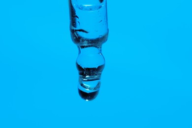 Photo of Dripping face serum from pipette on blue background, closeup