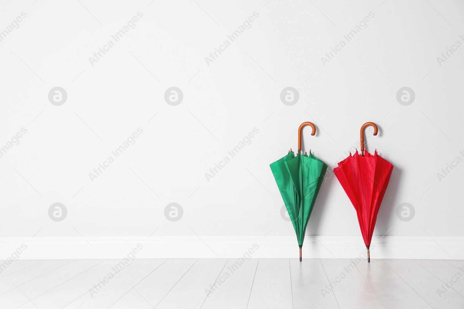 Photo of Beautiful bright umbrellas on floor near white wall with space for design