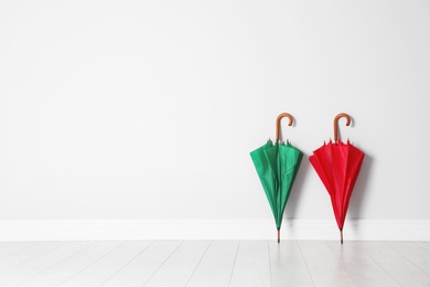 Photo of Beautiful bright umbrellas on floor near white wall with space for design