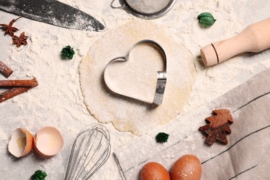 Flat lay composition with heart shaped cookie cutter, dough and ingredients on table
