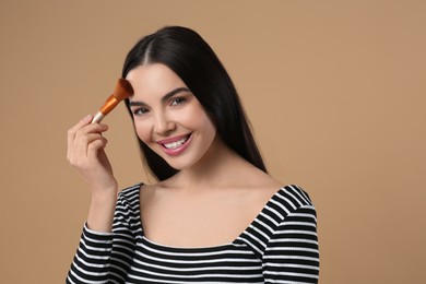 Happy woman applying makeup on light brown background. Space for text