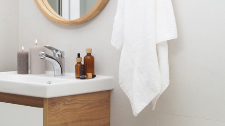 Photo of Hanging towel, sink, burning candles and toiletries in bathroom. Interior design