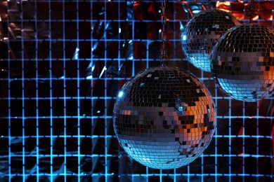Shiny disco balls against foil party curtain under color lights, space for text