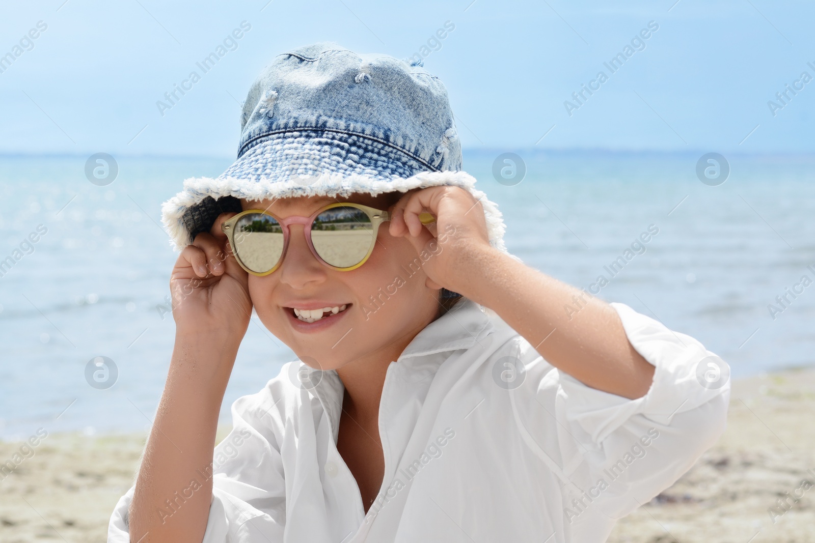 Photo of Little girl wearing sunglasses and hat at beach on sunny day