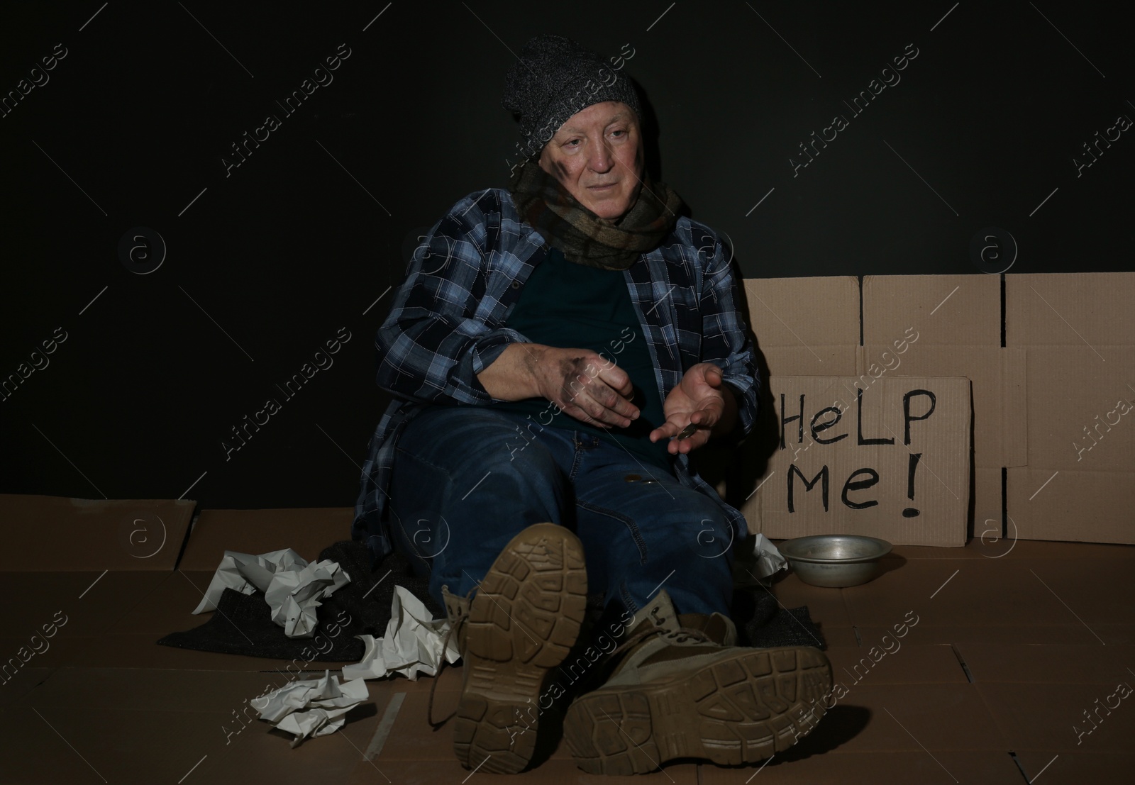 Photo of Poor senior man counting coins near cardboard sign HELP ME and dark wall