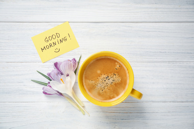 Delicious coffee, flowers and card with GOOD MORNING wish on white wooden table, flat lay