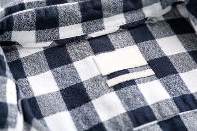 Photo of Blank clothing label on checkered shirt, closeup