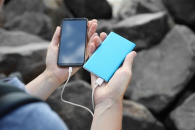 Photo of Woman charging smartphone with power bank on rocky mountain, closeup