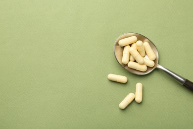 Photo of Vitamin capsules in spoon on olive background, top view. Space for text