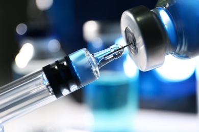 Photo of Filling syringe with vaccine from vial on blurred background, closeup