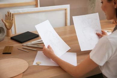 Photo of Young woman with portrait drawings at table indoors, closeup