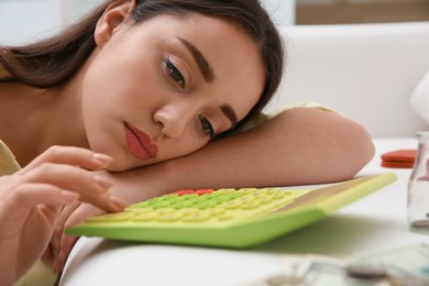 Sad woman counting money with calculator on sofa indoors